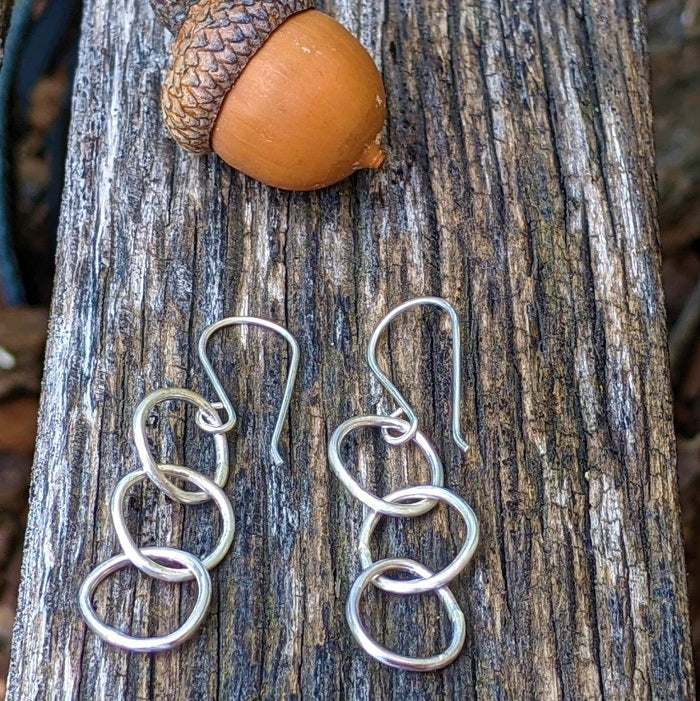 Sterling Silver Pebble Earrings lay on a rustic park bench near the Danare Designs studio.