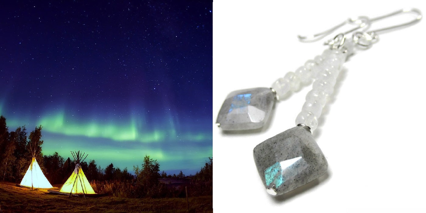 A pair of moonstone and labradorite earrings alongside people camping in tent under a dark sky filled with the northern lights